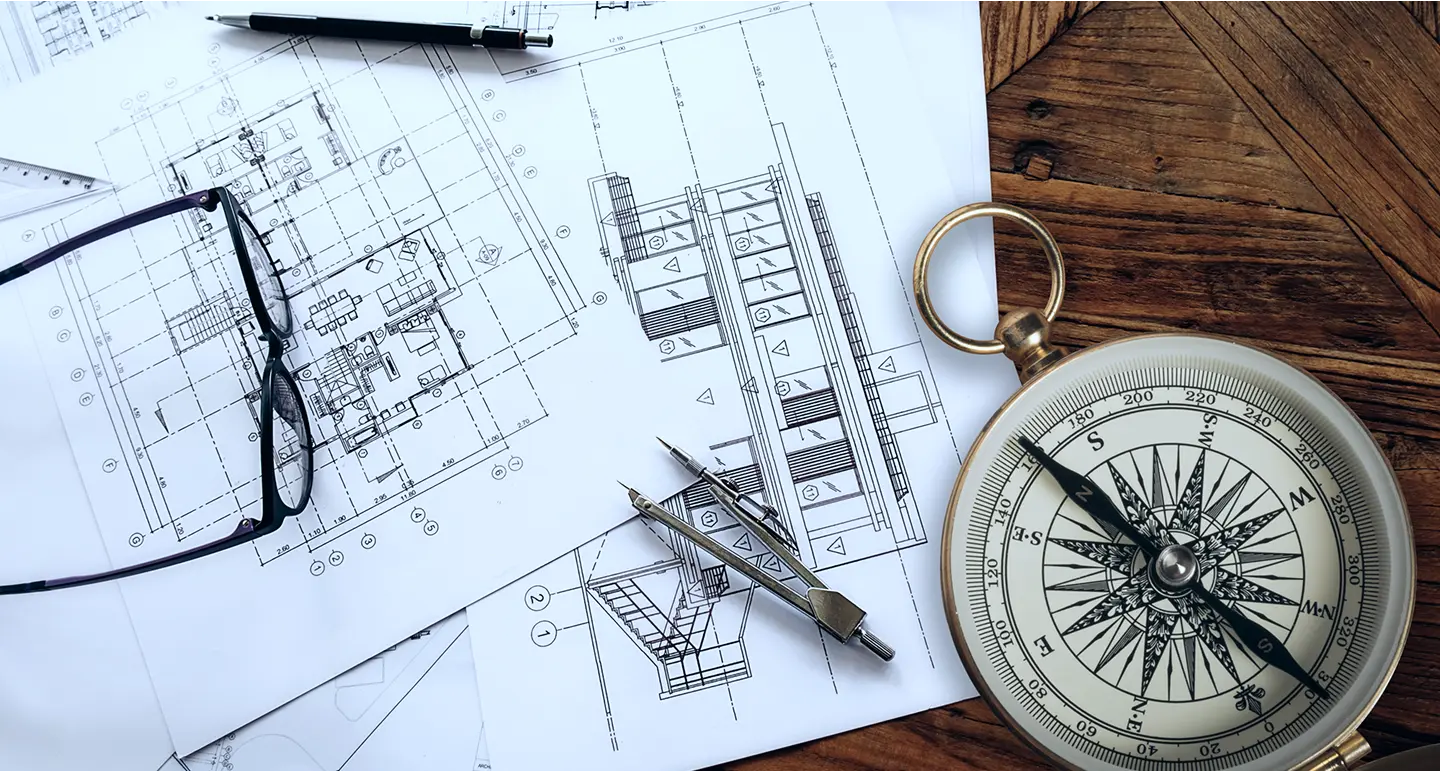 Architectural blueprints and compass for planning a commercial hub for lease in Delhi NCR.
