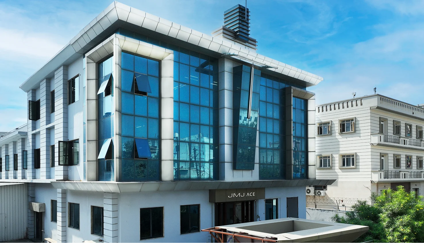 JMJ ACE manufacturing facility for rent in Tronica City Ghaziabad featuring a modern blue glass facade.