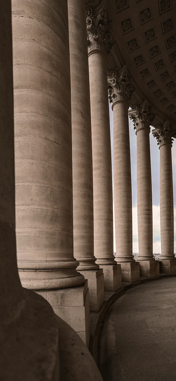 Perspective of a curved classical stone colonnade with Corinthian columns and coffered ceiling.