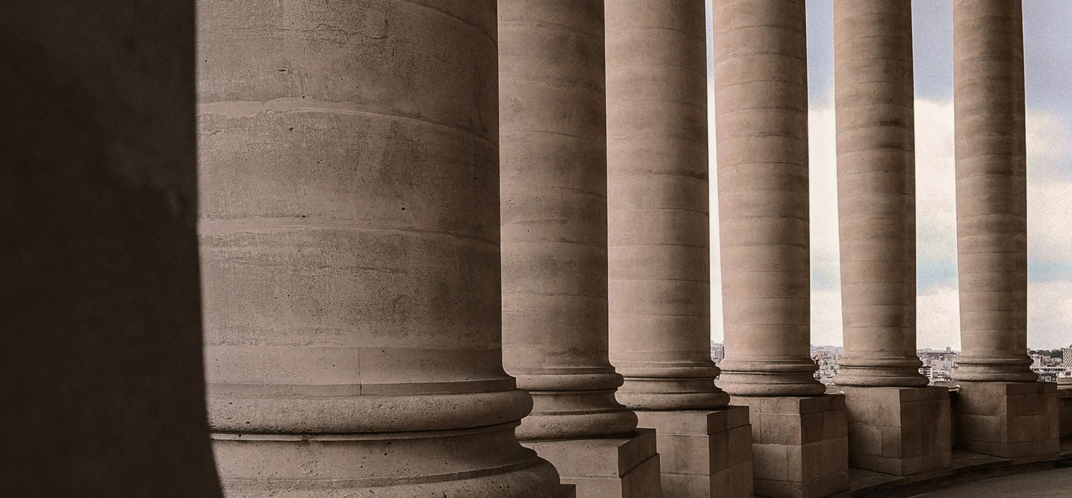 Row of classical stone columns receding in perspective overlooking a city skyline.